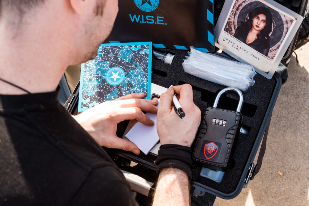 Jogador a tomar notas junto ao kit de agente da W.I.S.E., com um cadeado de código, no escape game Operation Mindfall