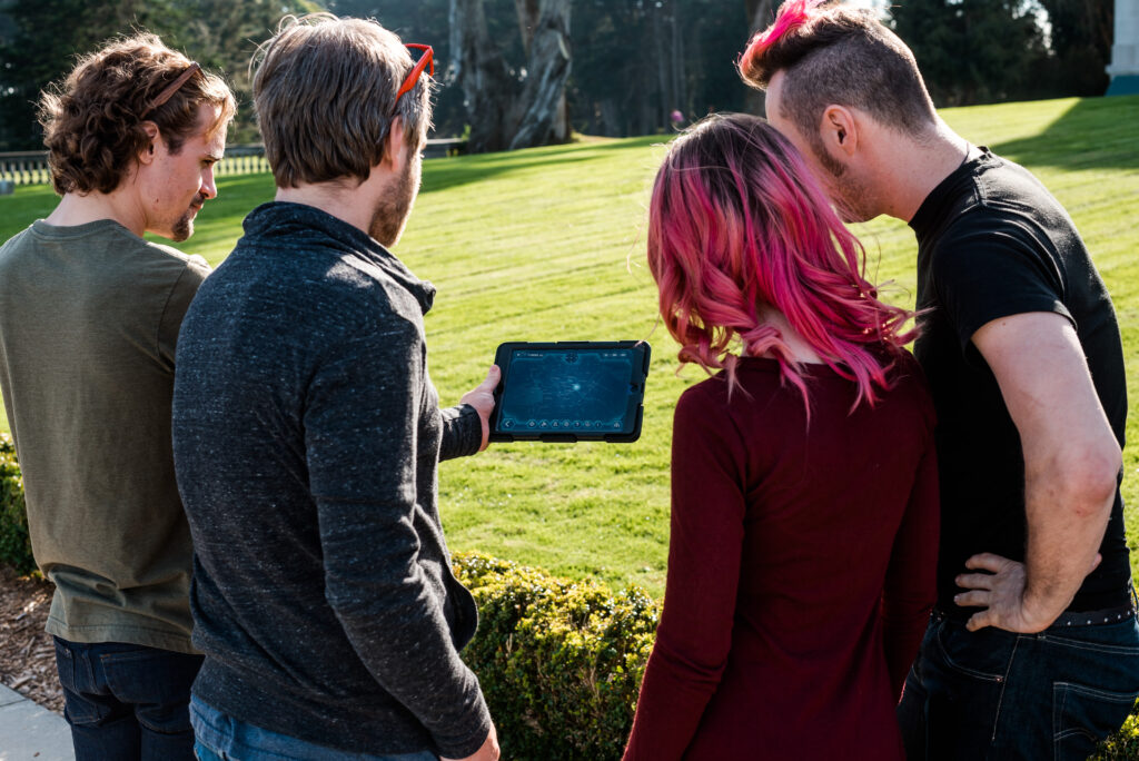 Equipa a consultar o iPad durante um escape game ao ar livre, num jardim